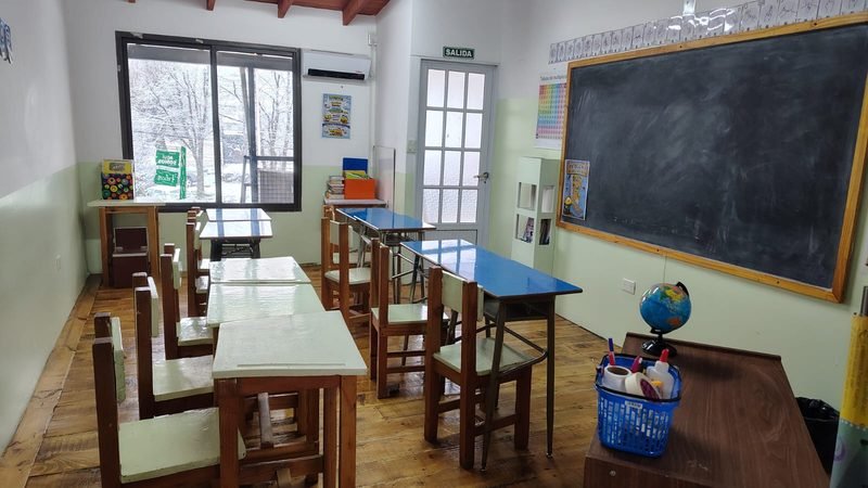 Aula con pizarrón, bancos de madera y un globo terráqueo sobre el escritorio, con la ventana nevada al fondo