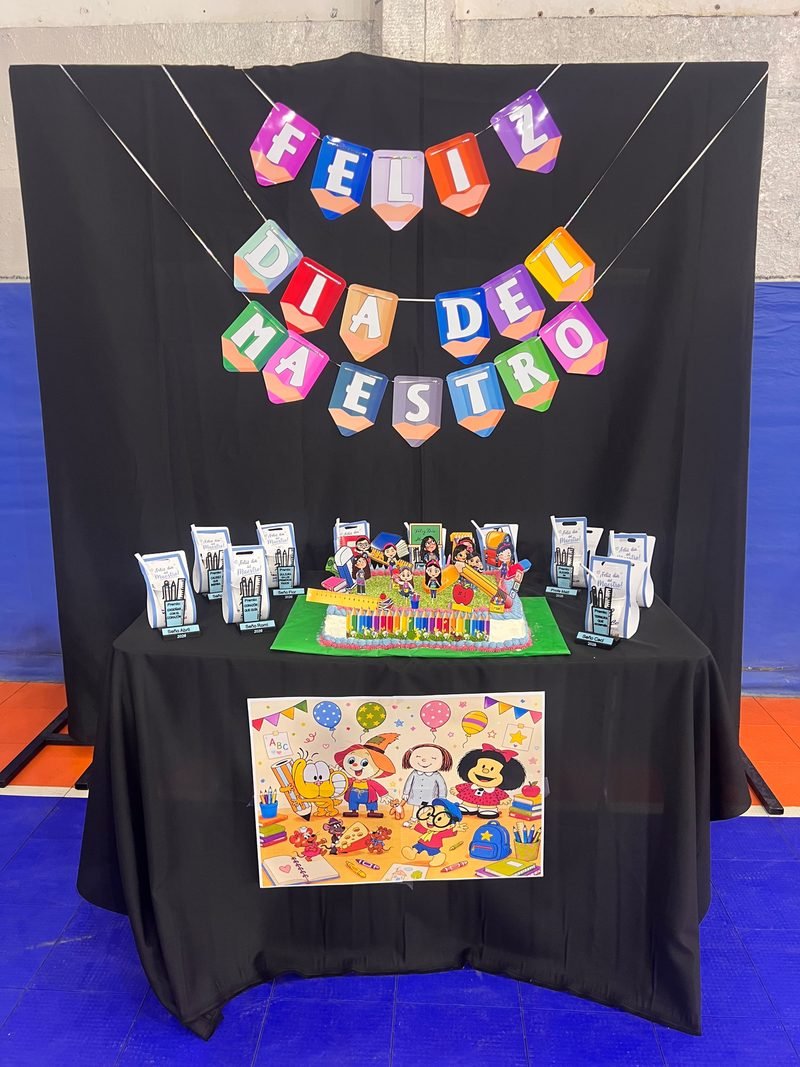 Mesa decorada para el Día del Maestro con guirnalda de colores, souvenirs y una lámina ilustrada