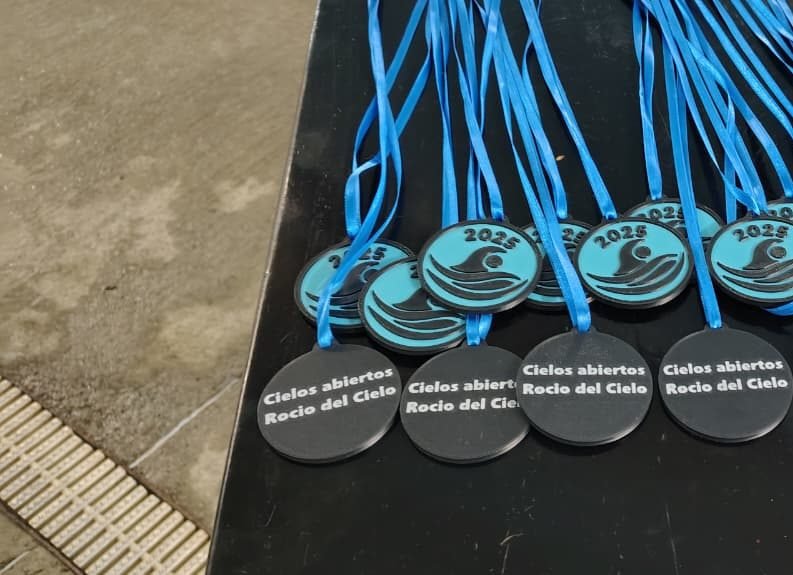 Medallas de natación 2025 de Cielos Abiertos y Rocío del Cielo con cintas celestes, sobre una mesa al borde de la pileta