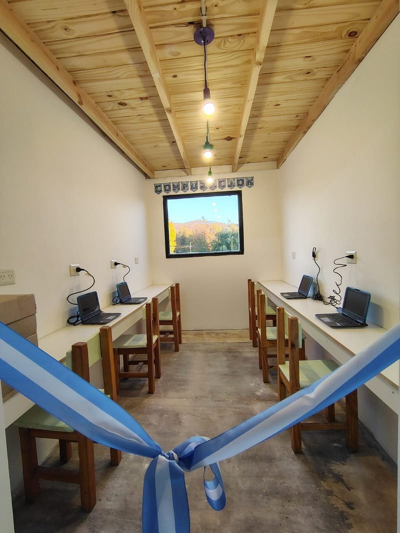 Sala de computación nueva con notebooks sobre mesas de madera y una cinta argentina de inauguración